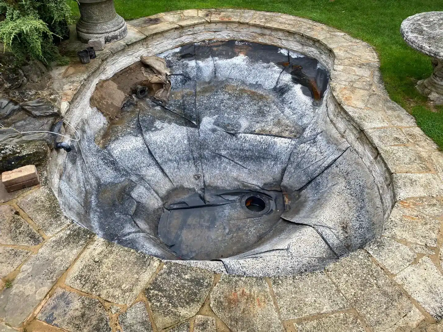 An existing pond with an old liner showing folds, creases, and wear, ready for fibreglass conversion.