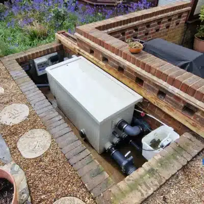 A Burtons BD300 Combi Drum Filter expertly installed by That Pond Guy in a concealed filter pit in Kent, ensuring efficient pond filtration and a clean setup.