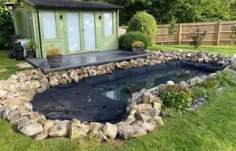 Leaking Pond Relined and Edged with Rocks by That Pond Guy A formerly leaking pond successfully relined by That Pond Guy, now enhanced with natural rock edging for an aesthetic and functional upgrade.
