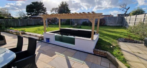 A premium koi pond built by That Pond Guy in Kent, featuring a sleek white rendered finish, a large viewing window, and a gazebo for a stylish design.