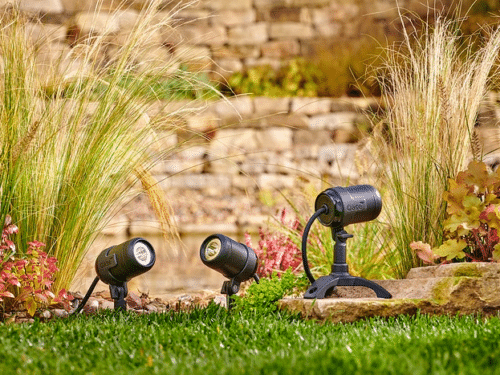 Three LunAqua Connect LED spotlights installed in a landscaped garden, illuminating plants and decorative features.