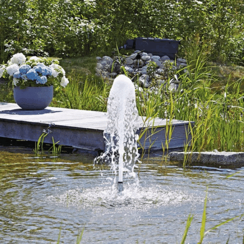 Oase Schaumsprudler 35 10 E fountain nozzle creating a tall vertical water jet in a landscaped garden pond with plants and decking.