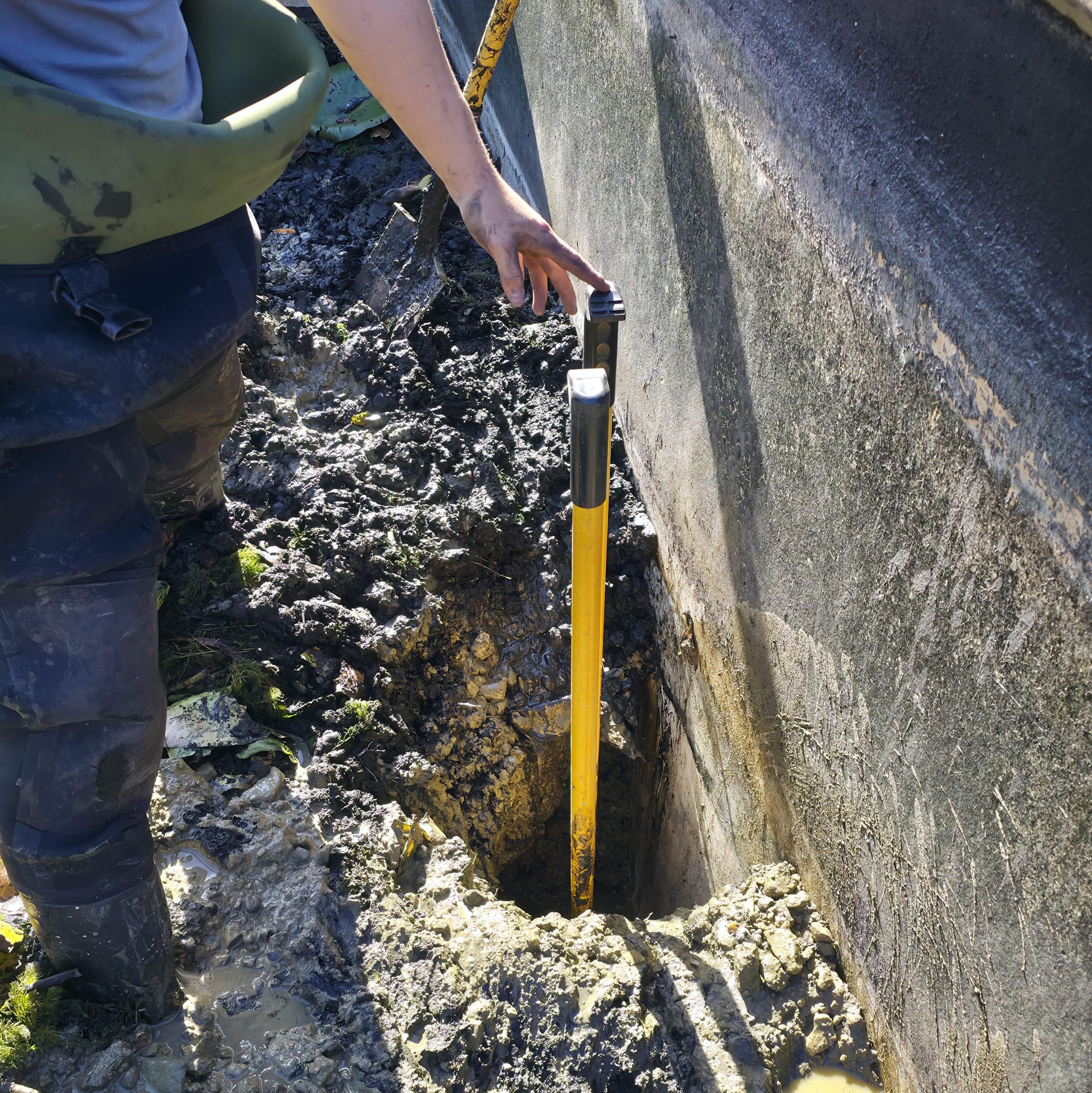 Team member showing the depth of compacted mud removed during the swimming pool turned pond renovation at Buckhurst Estate in Sussex