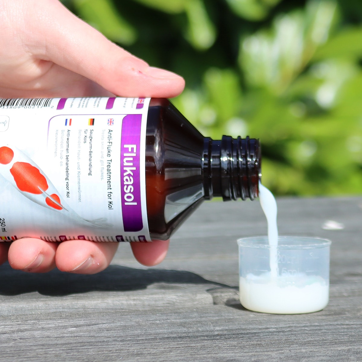 NT Labs Koi Care Flukasol 250ml bottle being measured for pond treatment